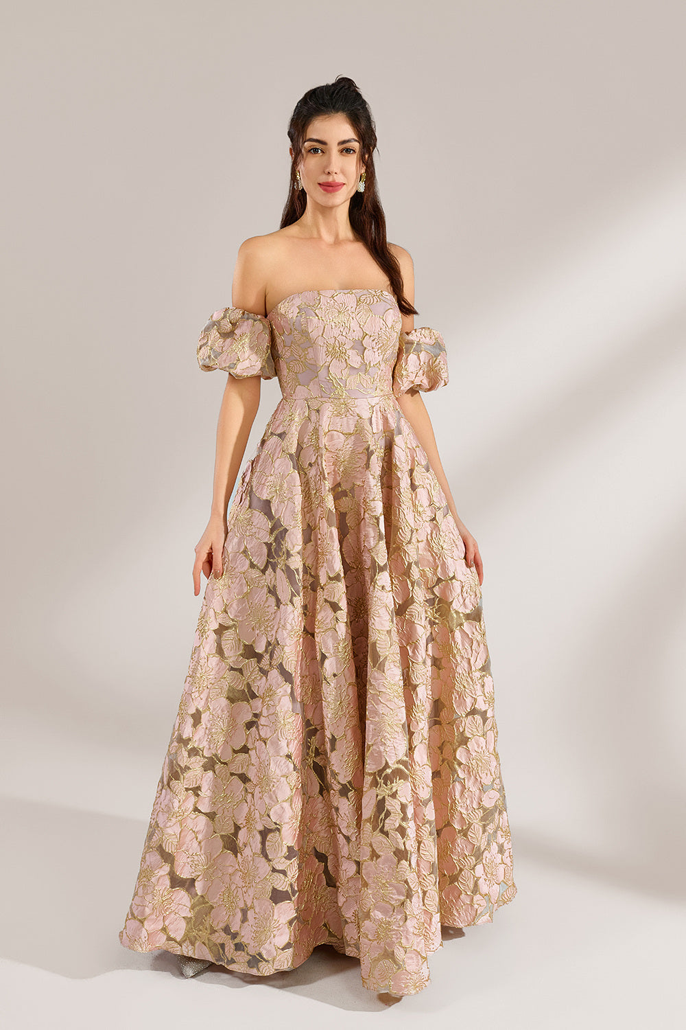 A woman with long, wavy dark hair and a poised stance wears a light - pink, floral - embroidered off - the - shoulder gown. It has puffed sleeves, a fitted bodice, and a voluminous skirt. Paired with understated heels, the outfit radiates elegance, perfect for formal events like galas or weddings.3
