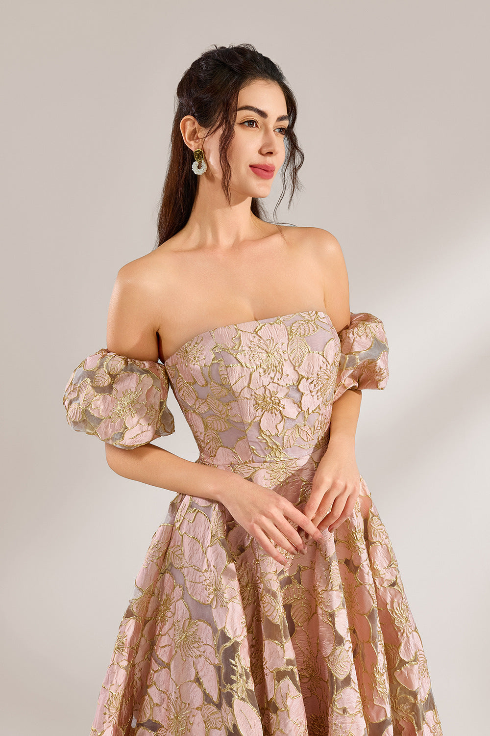A woman with long, wavy dark hair and a poised stance wears a light - pink, floral - embroidered off - the - shoulder gown. It has puffed sleeves, a fitted bodice, and a voluminous skirt. Paired with understated heels, the outfit radiates elegance, perfect for formal events like galas or weddings.6