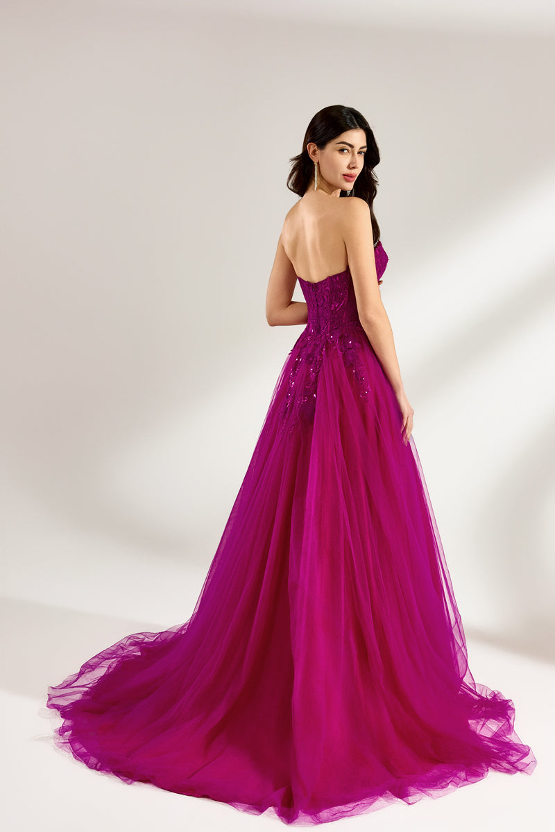 Photograph of a woman with long, dark hair in a strapless, vibrant magenta ball gown with a fitted bodice and a voluminous tulle skirt. The dress features a thigh-high slit on the left side and sparkling embellishments. She stands against a plain white background, exuding elegance and confidence.3321-02