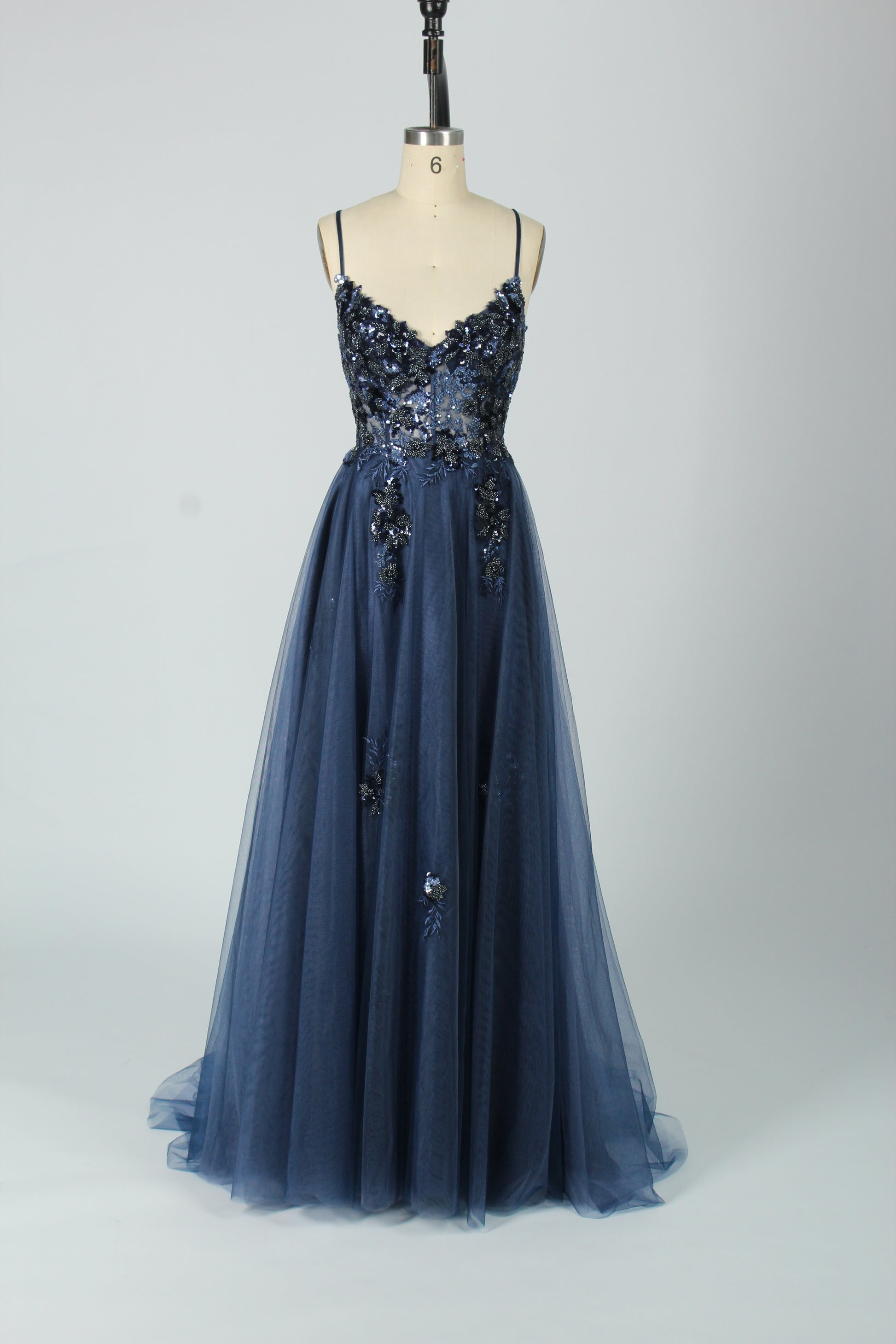 A woman stands against a light background, wearing a blue tulle gown. It features thin straps, a deep V - neckline, intricate floral appliqués with sequins on the bodice, and a high side slit. The voluminous tulle skirt creates a romantic and glamorous look, perfect for formal events like proms or weddings.7