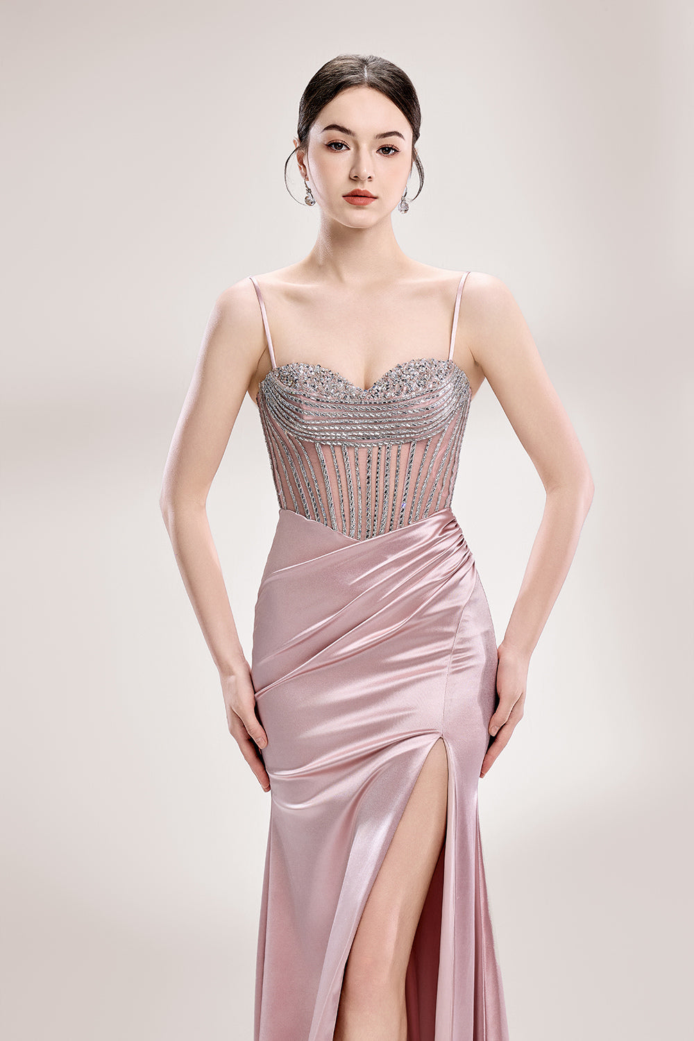 A woman stands against a light background, wearing a pink satin gown with a beaded, sheer bodice. It has thin straps, a ruched skirt, and a high side slit. The contrast of the sparkling beads and smooth satin fabric exudes elegance, perfect for formal galas or evening events, radiating charm.3