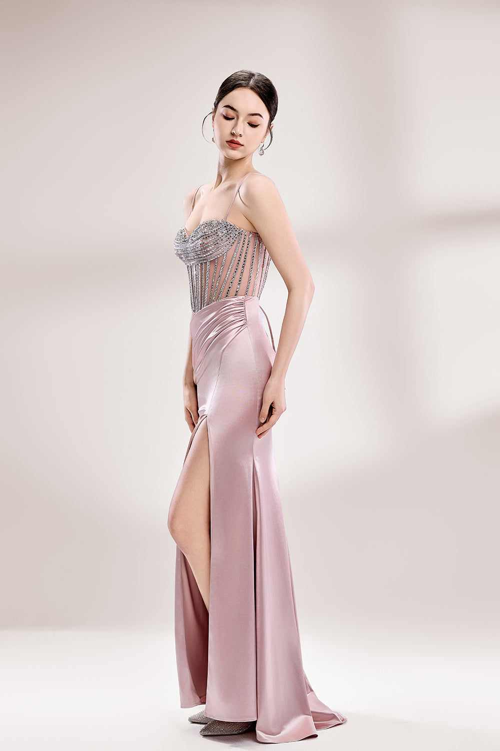 A woman stands against a light background, wearing a pink satin gown with a beaded, sheer bodice. It has thin straps, a ruched skirt, and a high side slit. The contrast of the sparkling beads and smooth satin fabric exudes elegance, perfect for formal galas or evening events, radiating charm.4