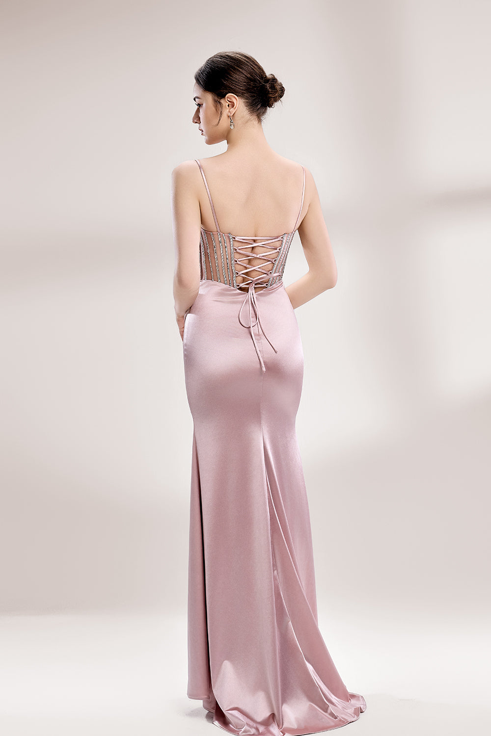 A woman stands against a light background, wearing a pink satin gown with a beaded, sheer bodice. It has thin straps, a ruched skirt, and a high side slit. The contrast of the sparkling beads and smooth satin fabric exudes elegance, perfect for formal galas or evening events, radiating charm.2