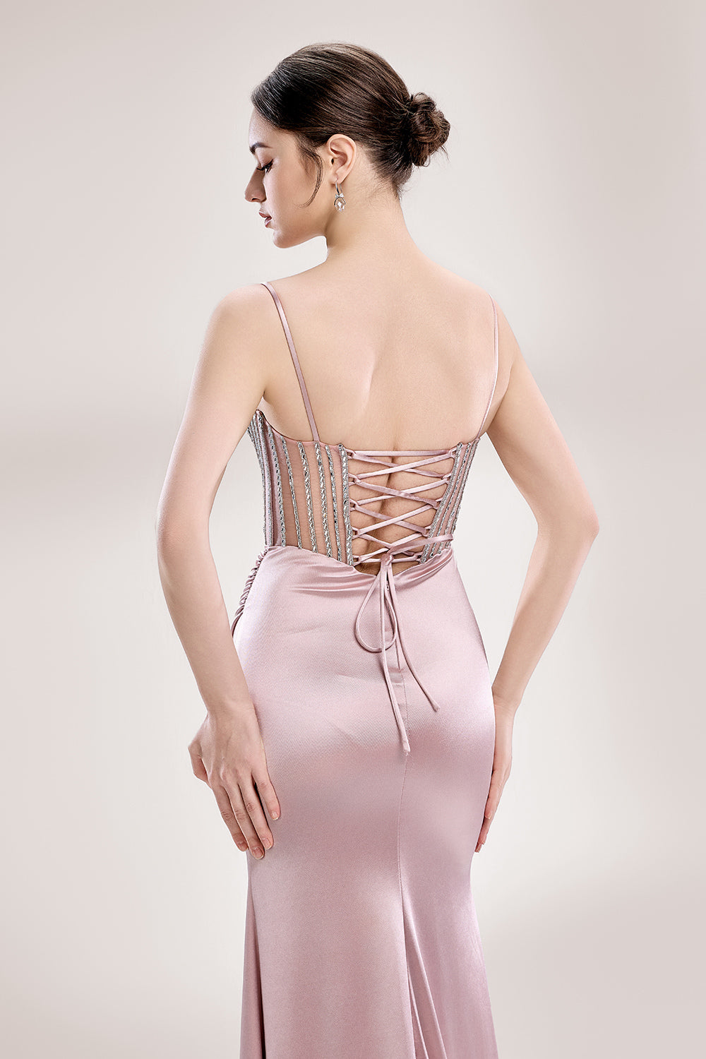 A woman stands against a light background, wearing a pink satin gown with a beaded, sheer bodice. It has thin straps, a ruched skirt, and a high side slit. The contrast of the sparkling beads and smooth satin fabric exudes elegance, perfect for formal galas or evening events, radiating charm.6