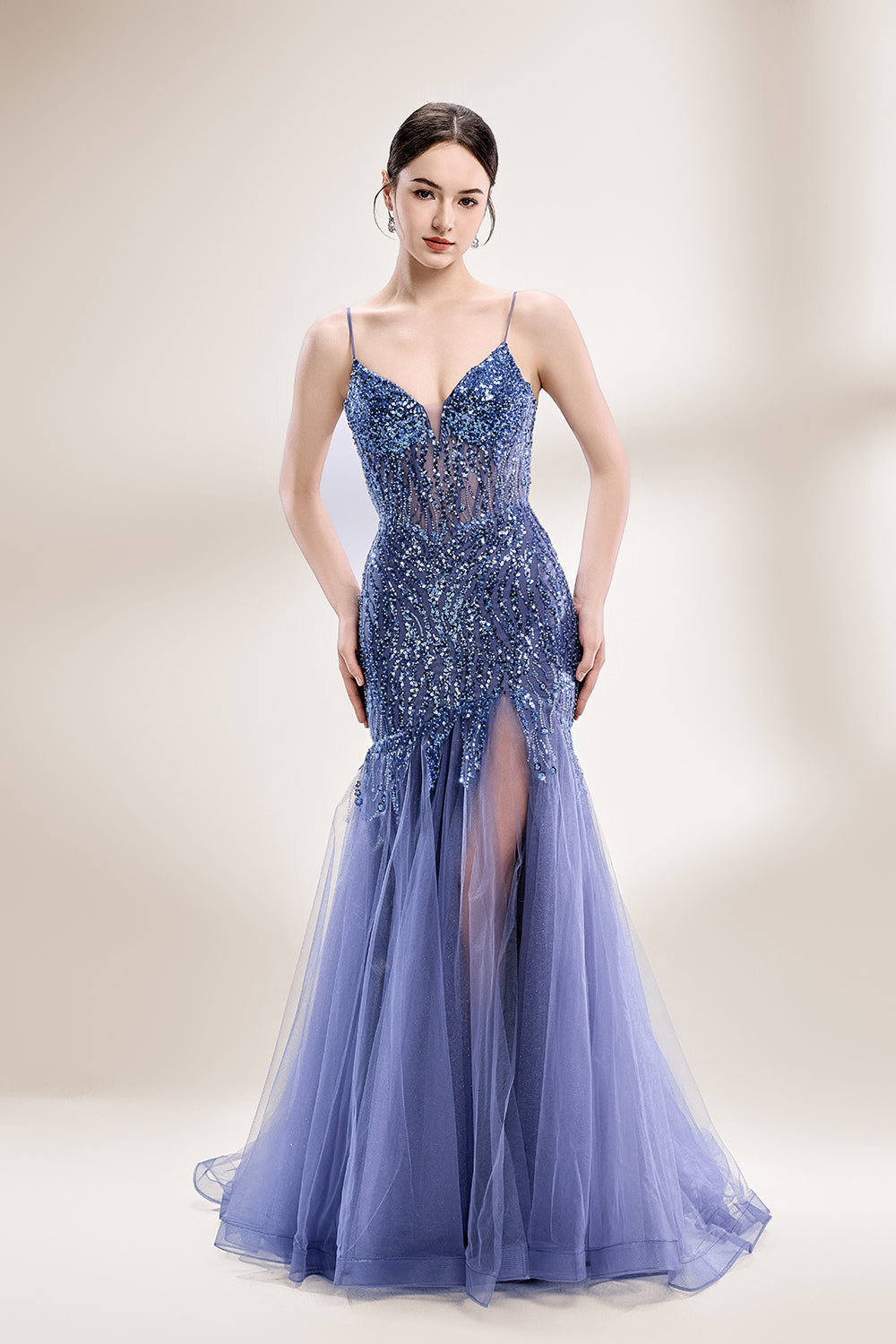 Photograph of a young Asian woman with fair skin and dark hair in a sleek bun, wearing a stunning, floor-length, deep blue evening gown. The gown has a plunging V-neckline, adorned with intricate beading and sequins, and features a sheer overlay with a high slit on one side, revealing a layer of tulle. The background is a soft, neutral gradient, highlighting the gown's elegance. She accessorizes with large, dangling earrings.1