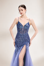 Photograph of a young Asian woman with fair skin and dark hair in a sleek bun, wearing a stunning, floor-length, deep blue evening gown. The gown has a plunging V-neckline, adorned with intricate beading and sequins, and features a sheer overlay with a high slit on one side, revealing a layer of tulle. The background is a soft, neutral gradient, highlighting the gown's elegance. She accessorizes with large, dangling earrings.4