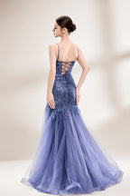 Photograph of a young Asian woman with fair skin and dark hair in a sleek bun, wearing a stunning, floor-length, deep blue evening gown. The gown has a plunging V-neckline, adorned with intricate beading and sequins, and features a sheer overlay with a high slit on one side, revealing a layer of tulle. The background is a soft, neutral gradient, highlighting the gown's elegance. She accessorizes with large, dangling earrings.2