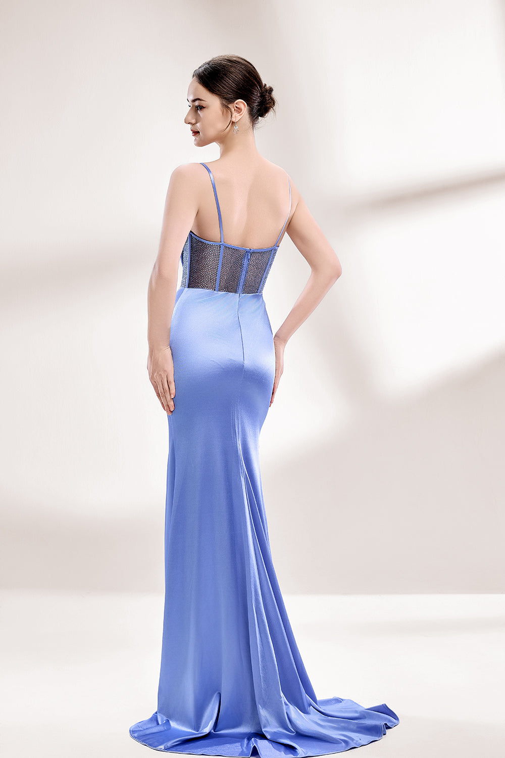 A woman with sleek dark hair and a poised stance wears a light - blue satin gown. It has thin straps, a cowl neckline, sheer mesh side panels, and a high side slit. Paired with understated earrings, the outfit radiates elegance, perfect for formal events like galas or evening receptions.2