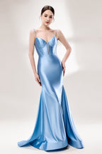 Photograph of a slender, fair-skinned woman with dark hair in an elegant updo, wearing a stunning, floor-length, light blue satin gown with a plunging neckline and thin spaghetti straps. The dress features a fitted bodice and a flowing skirt. She stands against a plain, light gray background, with soft lighting emphasizing the gown's sheen.1