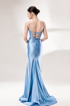 Photograph of a slender, fair-skinned woman with dark hair in an elegant updo, wearing a stunning, floor-length, light blue satin gown with a plunging neckline and thin spaghetti straps. The dress features a fitted bodice and a flowing skirt. She stands against a plain, light gray background, with soft lighting emphasizing the gown's sheen.5