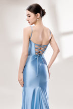 Photograph of a slender, fair-skinned woman with dark hair in an elegant updo, wearing a stunning, floor-length, light blue satin gown with a plunging neckline and thin spaghetti straps. The dress features a fitted bodice and a flowing skirt. She stands against a plain, light gray background, with soft lighting emphasizing the gown's sheen.6