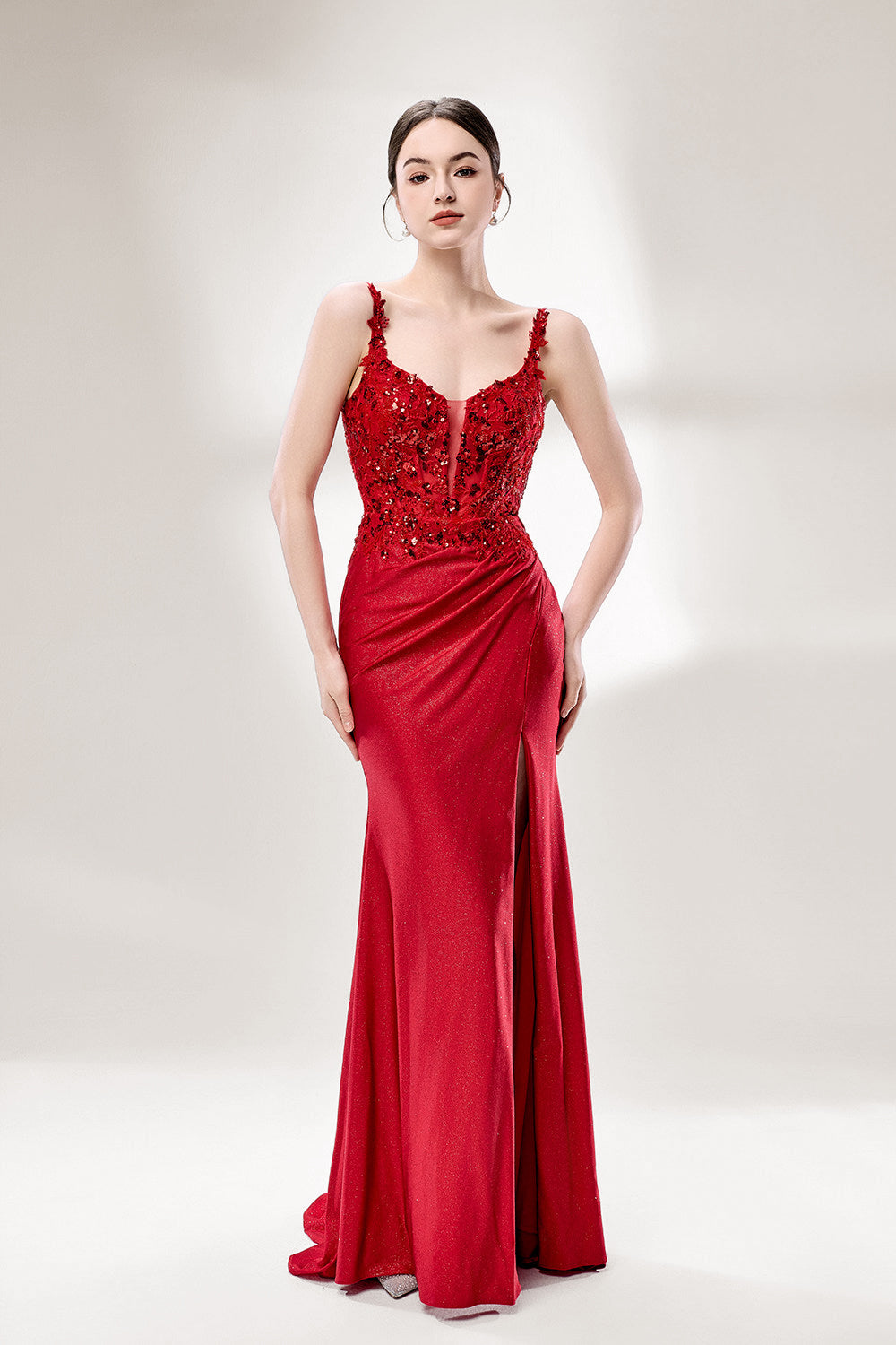 A woman with sleek dark hair and a poised stance wears a red, glittery gown. It has thin straps, beaded bodice, and a high side slit. Paired with silver heels, the outfit radiates elegance, perfect for formal events like galas, blending glamour and style.
6