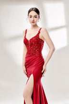 A woman with sleek dark hair and a poised stance wears a red, glittery gown. It has thin straps, beaded bodice, and a high side slit. Paired with silver heels, the outfit radiates elegance, perfect for formal events like galas, blending glamour and style.
