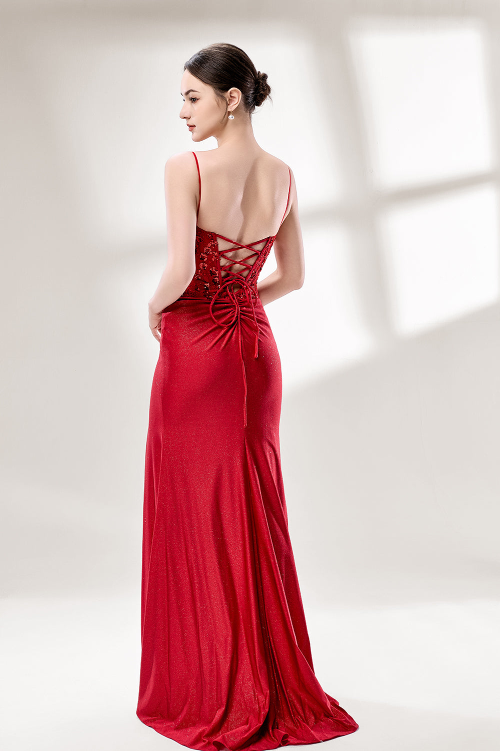 A woman with sleek dark hair and a poised stance wears a red, glittery gown. It has thin straps, beaded bodice, and a high side slit. Paired with silver heels, the outfit radiates elegance, perfect for formal events like galas, blending glamour and style.
2