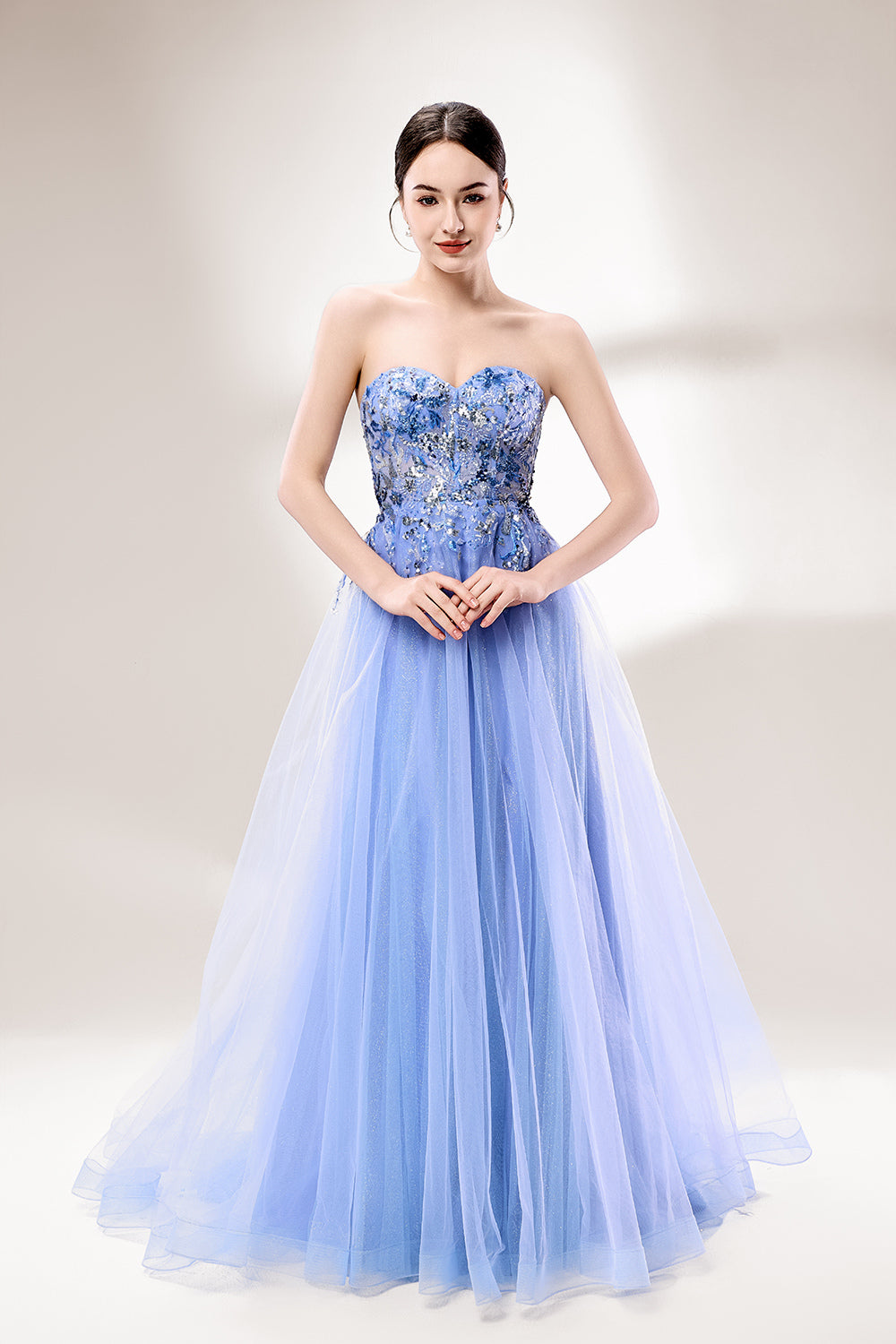 Set against a light background, a woman wears a light blue strapless ball gown. It features a sweetheart neckline with intricate floral beadwork on the bodice, and a voluminous tulle skirt. The elegant design creates a romantic and dreamy look, perfect for formal events like proms or weddings.1