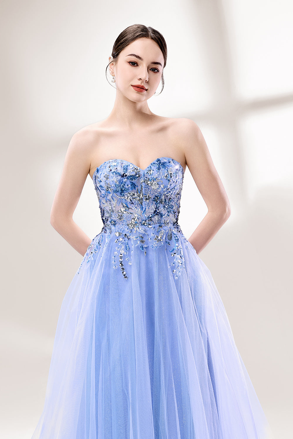 Set against a light background, a woman wears a light blue strapless ball gown. It features a sweetheart neckline with intricate floral beadwork on the bodice, and a voluminous tulle skirt. The elegant design creates a romantic and dreamy look, perfect for formal events like proms or weddings.3