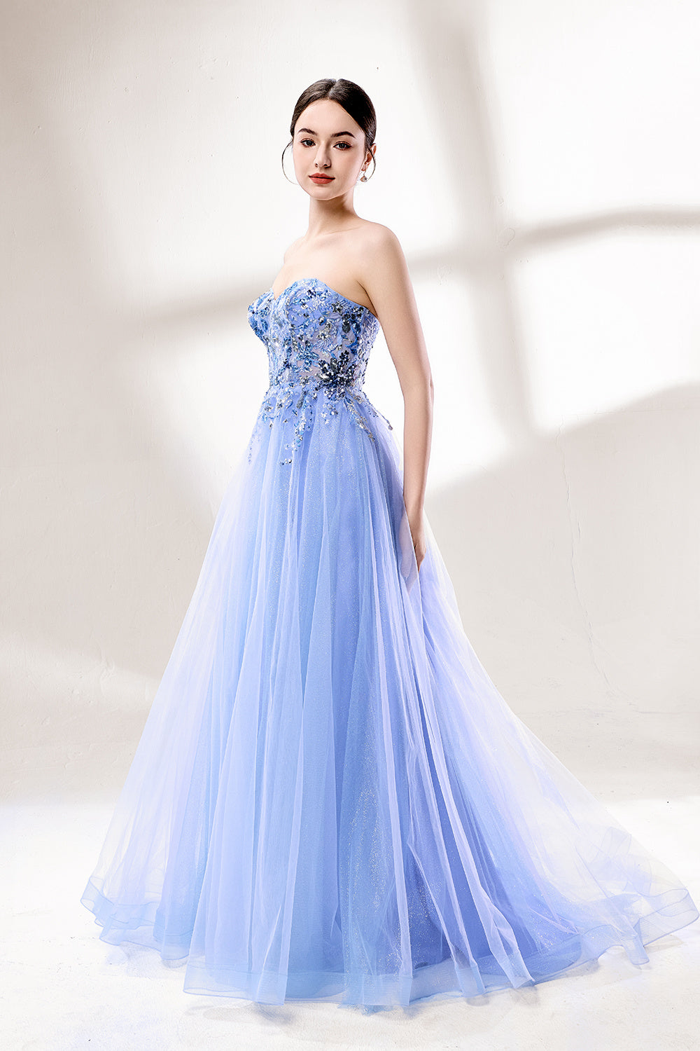 Set against a light background, a woman wears a light blue strapless ball gown. It features a sweetheart neckline with intricate floral beadwork on the bodice, and a voluminous tulle skirt. The elegant design creates a romantic and dreamy look, perfect for formal events like proms or weddings.4