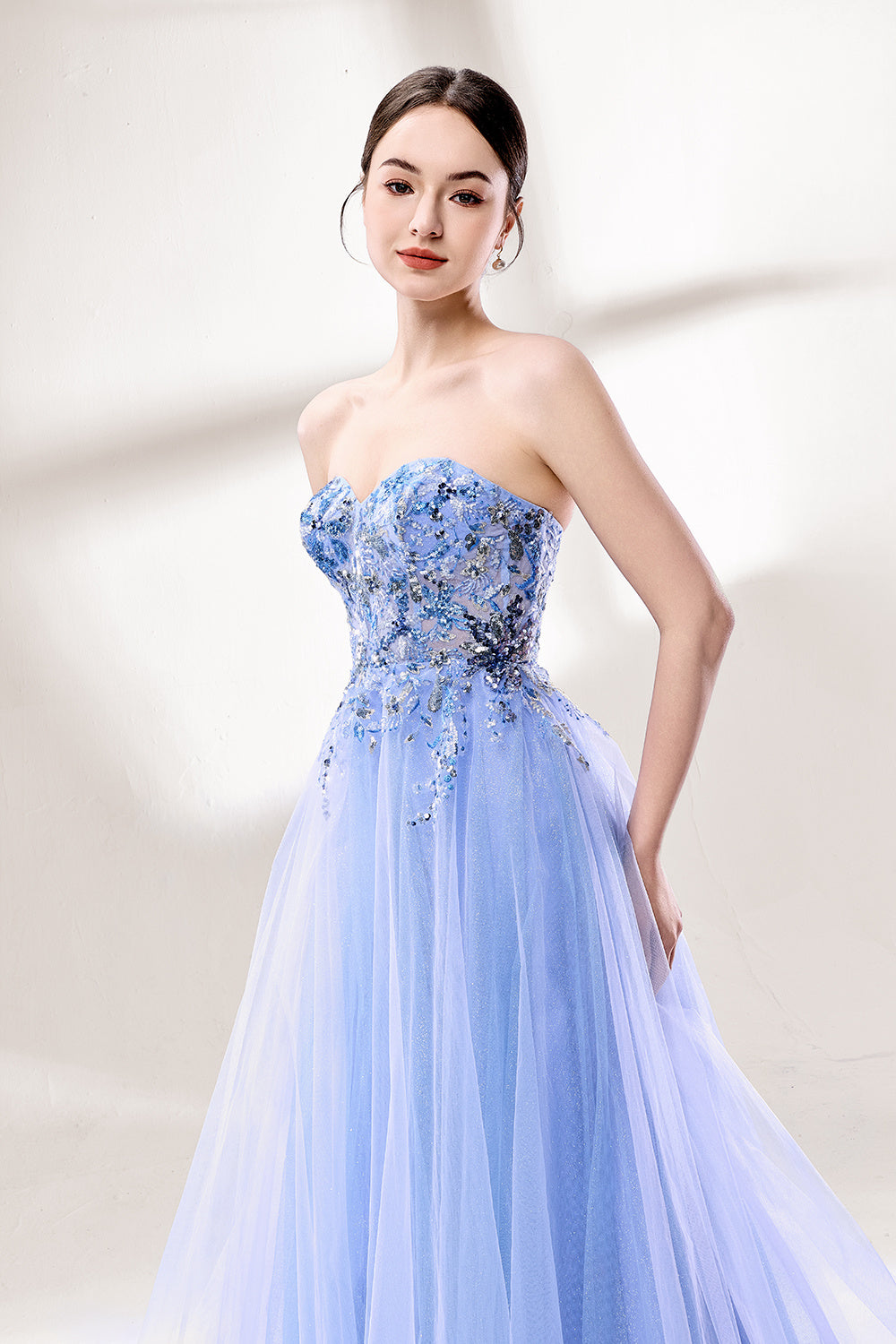 Set against a light background, a woman wears a light blue strapless ball gown. It features a sweetheart neckline with intricate floral beadwork on the bodice, and a voluminous tulle skirt. The elegant design creates a romantic and dreamy look, perfect for formal events like proms or weddings.5