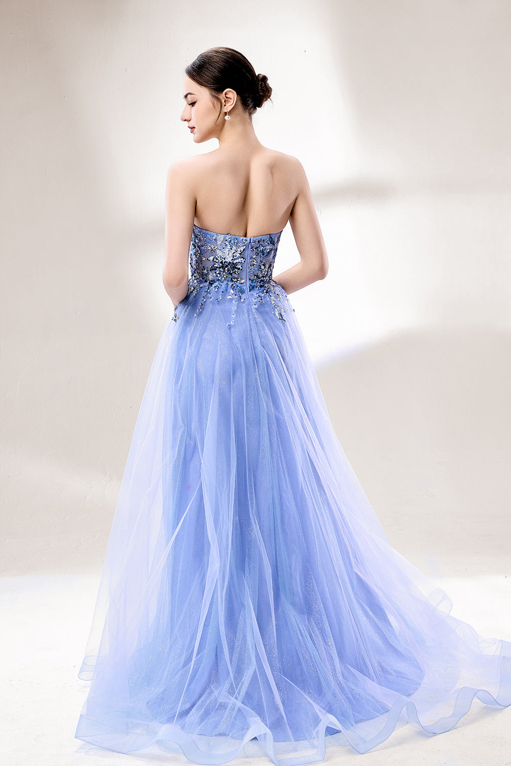Set against a light background, a woman wears a light blue strapless ball gown. It features a sweetheart neckline with intricate floral beadwork on the bodice, and a voluminous tulle skirt. The elegant design creates a romantic and dreamy look, perfect for formal events like proms or weddings.2