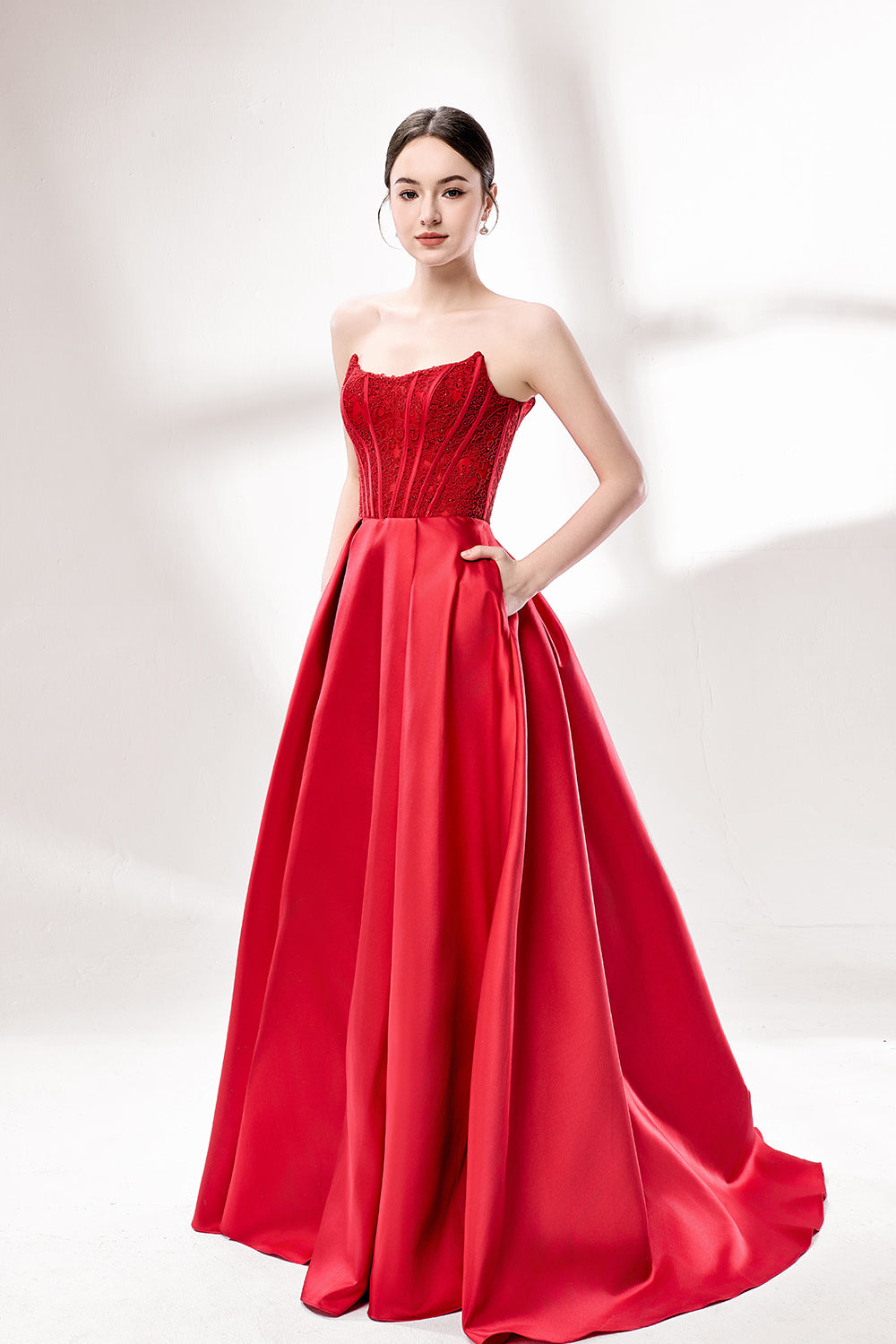 Against a light - hued background, a woman wears a red satin gown with a strapless, lace - detailed bodice and pockets. It has a voluminous skirt, combining romance and functionality. The vibrant red color and elegant design radiate confidence, perfect for formal events like weddings or award ceremonies.3