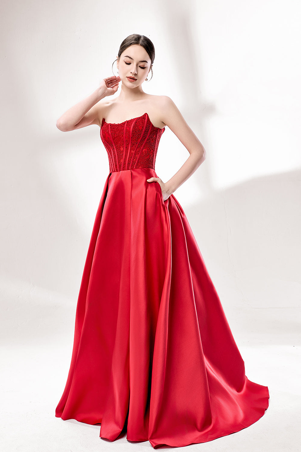Against a light - hued background, a woman wears a red satin gown with a strapless, lace - detailed bodice and pockets. It has a voluminous skirt, combining romance and functionality. The vibrant red color and elegant design radiate confidence, perfect for formal events like weddings or award ceremonies.4