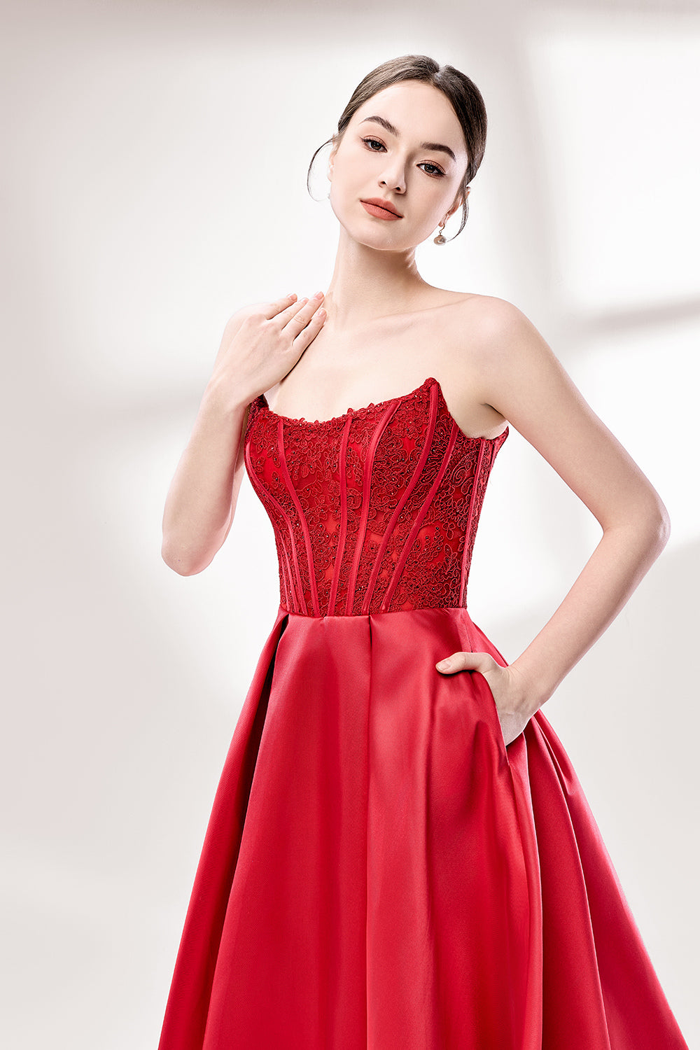 Against a light - hued background, a woman wears a red satin gown with a strapless, lace - detailed bodice and pockets. It has a voluminous skirt, combining romance and functionality. The vibrant red color and elegant design radiate confidence, perfect for formal events like weddings or award ceremonies.5