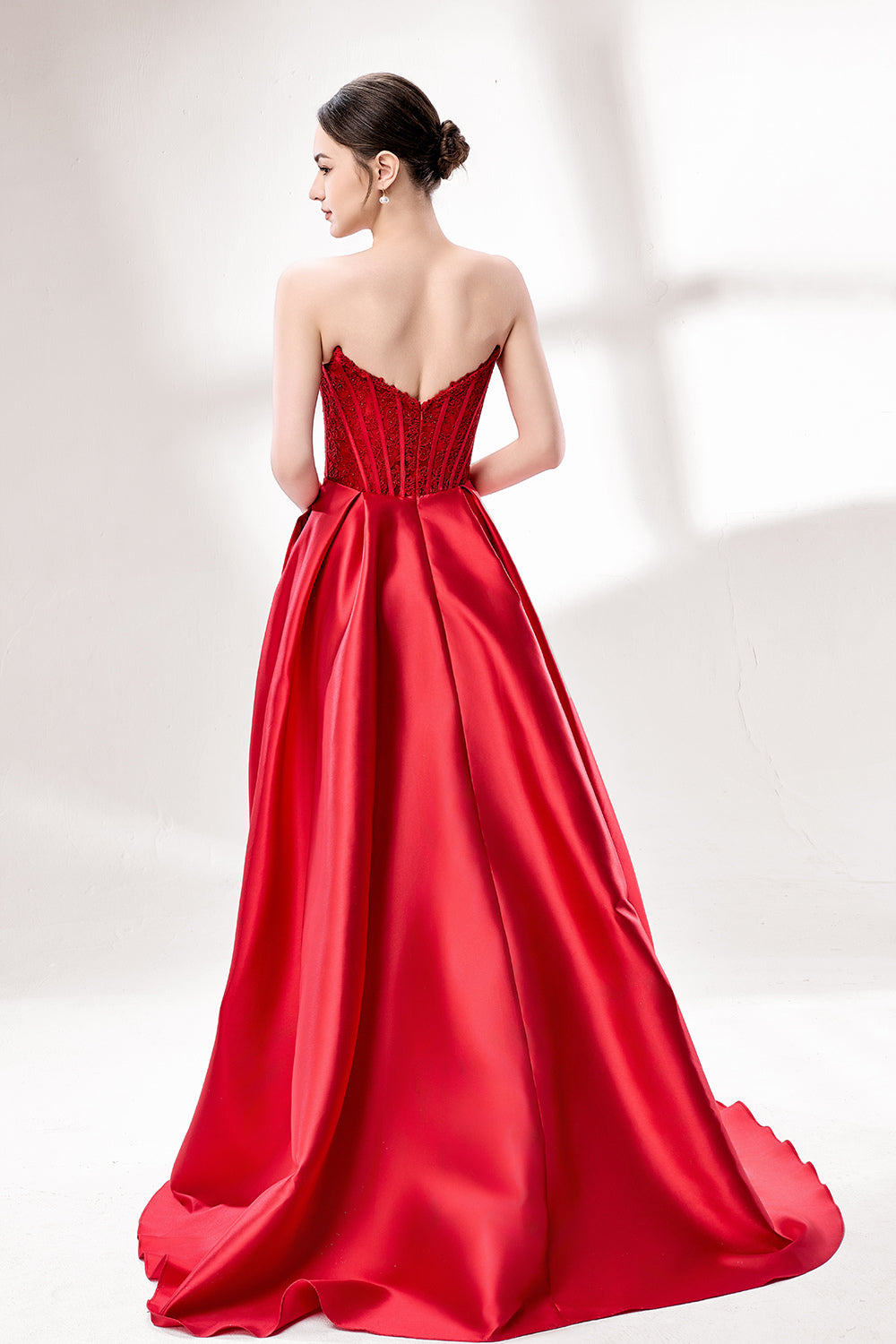 Against a light - hued background, a woman wears a red satin gown with a strapless, lace - detailed bodice and pockets. It has a voluminous skirt, combining romance and functionality. The vibrant red color and elegant design radiate confidence, perfect for formal events like weddings or award ceremonies.2