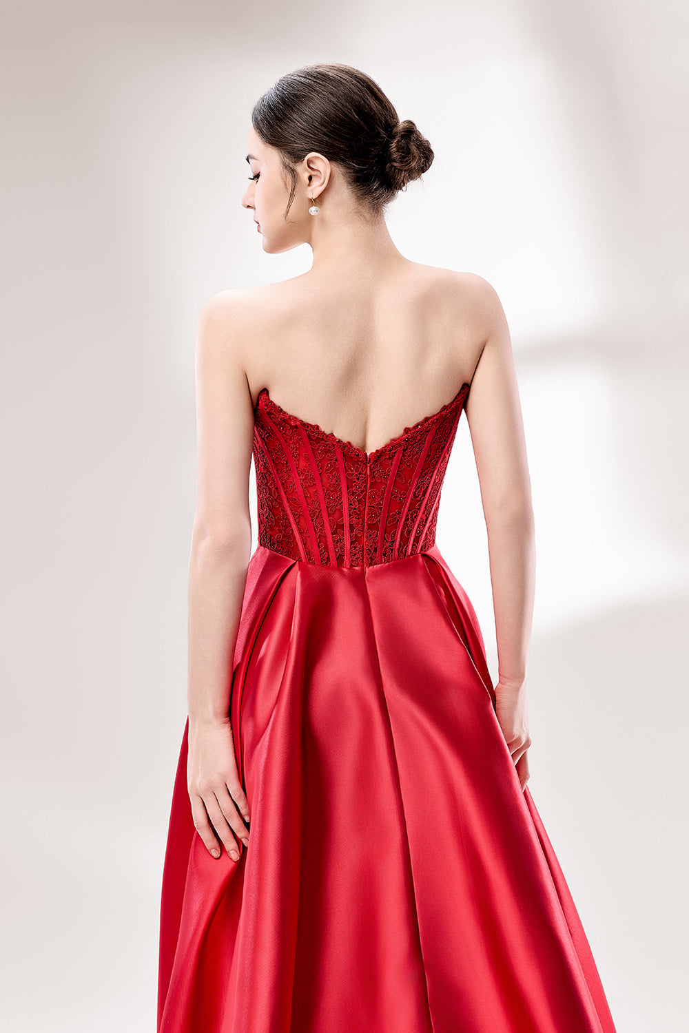 Against a light - hued background, a woman wears a red satin gown with a strapless, lace - detailed bodice and pockets. It has a voluminous skirt, combining romance and functionality. The vibrant red color and elegant design radiate confidence, perfect for formal events like weddings or award ceremonies.6