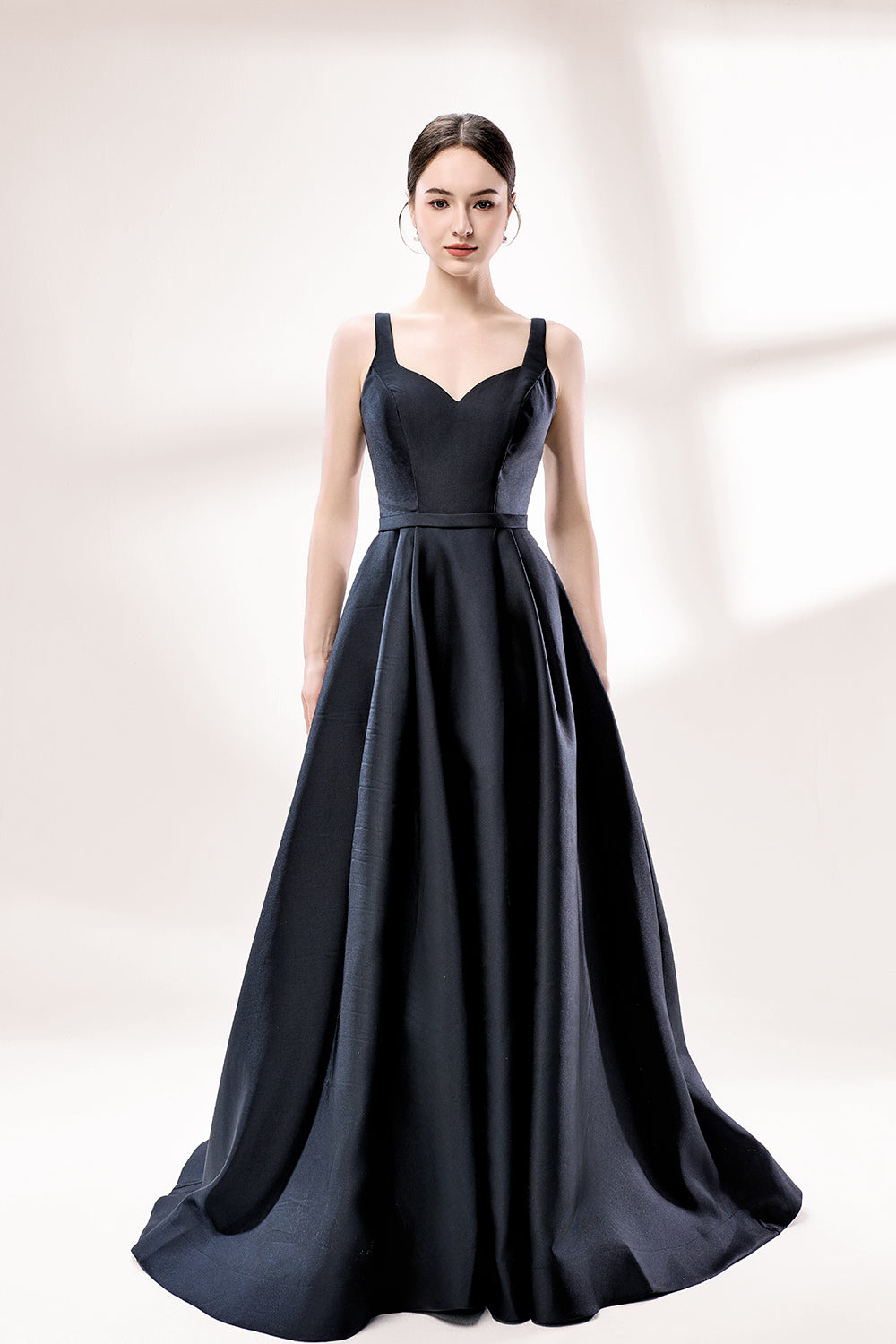 A woman stands against a light background, wearing a black satin gown. It features thin straps, a V - neckline, and a high side slit. The smooth satin fabric and elegant silhouette exude sophistication, perfect for formal events like galas or charity balls, radiating timeless charm.3
