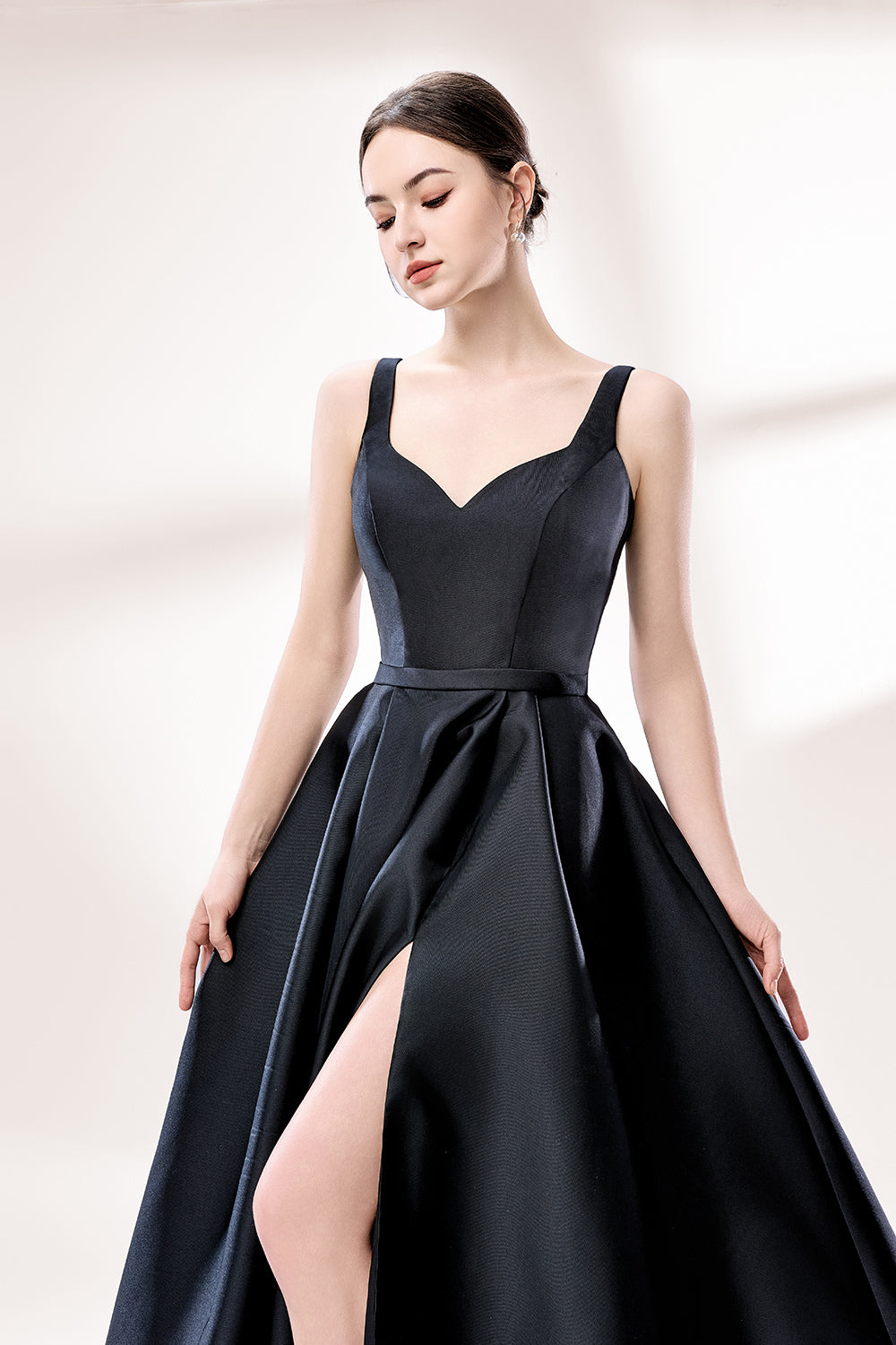 A woman stands against a light background, wearing a black satin gown. It features thin straps, a V - neckline, and a high side slit. The smooth satin fabric and elegant silhouette exude sophistication, perfect for formal events like galas or charity balls, radiating timeless charm.4