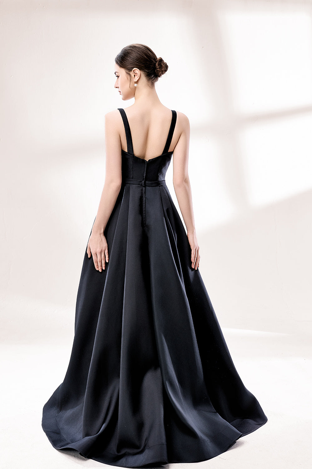 A woman stands against a light background, wearing a black satin gown. It features thin straps, a V - neckline, and a high side slit. The smooth satin fabric and elegant silhouette exude sophistication, perfect for formal events like galas or charity balls, radiating timeless charm.2