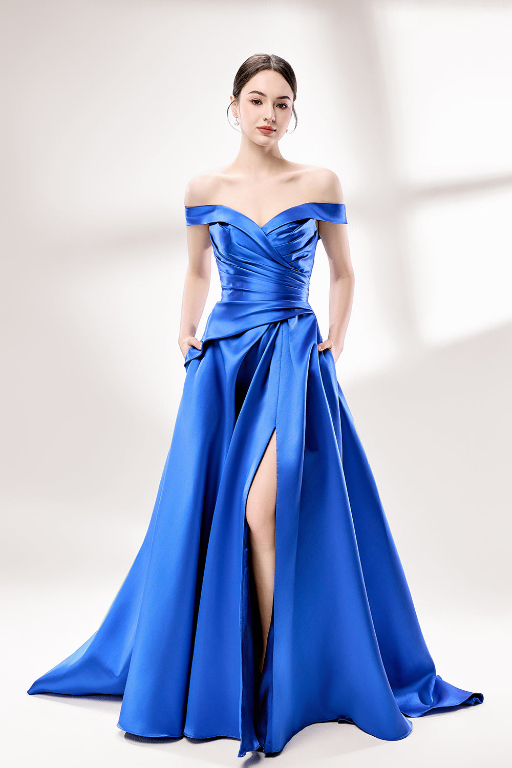 Set against a light backdrop, a woman dons a royal - blue satin gown with an off - shoulder neckline and a high side slit. It has a ruched bodice and pockets, combining elegance and practicality. The shiny satin fabric creates a glamorous look, ideal for proms or formal evening gatherings.1
