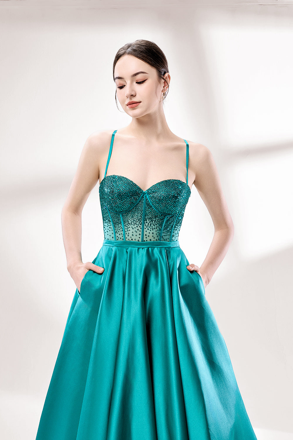 A woman stands against a light background, wearing a teal satin gown. It has thin straps, a sweetheart neckline, and a voluminous skirt. The bodice features sheer fabric with bead embellishments, combining elegance and romance. Perfect for formal events like weddings, it exudes charm.4