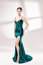 Set against a light background, a woman wears a teal satin gown with a bejeweled, sheer bodice. It has thin straps, a sweetheart neckline, and a mermaid - shaped skirt with a high side slit. The sparkling embellishments and smooth satin fabric exude elegance, ideal for galas or formal dinners.4