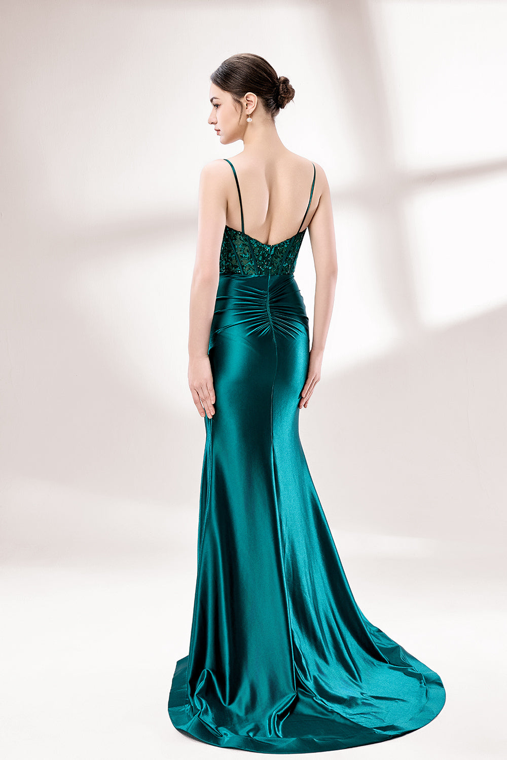 Set against a light background, a woman wears a teal satin gown with a bejeweled, sheer bodice. It has thin straps, a sweetheart neckline, and a mermaid - shaped skirt with a high side slit. The sparkling embellishments and smooth satin fabric exude elegance, ideal for galas or formal dinners.2