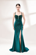 Photograph of a young Caucasian woman with fair skin and dark brown hair styled in an elegant updo. She is wearing a stunning, floor-length, teal evening gown with a deep V-neckline adorned with intricate beadwork. The gown features a high slit on the left, showcasing her slender legs. The fabric has a smooth, shimmering texture. The background is a soft, white gradient, creating a minimalist and elegant atmosphere. The overall style is sophisticated and glamorous, suitable for formal events.1