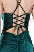 Photograph of a young Caucasian woman with fair skin and dark brown hair styled in an elegant updo. She is wearing a stunning, floor-length, teal evening gown with a deep V-neckline adorned with intricate beadwork. The gown features a high slit on the left, showcasing her slender legs. The fabric has a smooth, shimmering texture. The background is a soft, white gradient, creating a minimalist and elegant atmosphere. The overall style is sophisticated and glamorous, suitable for formal events.5