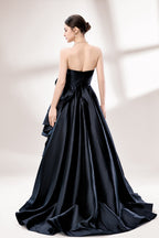Bathed in soft light, a woman dazzles in a black strapless ball gown. It features a sweetheart neckline, a large ruffled floral detail on the side, and a voluminous skirt. The elegant design creates a sophisticated and glamorous look, perfect for formal events like galas or weddings.5