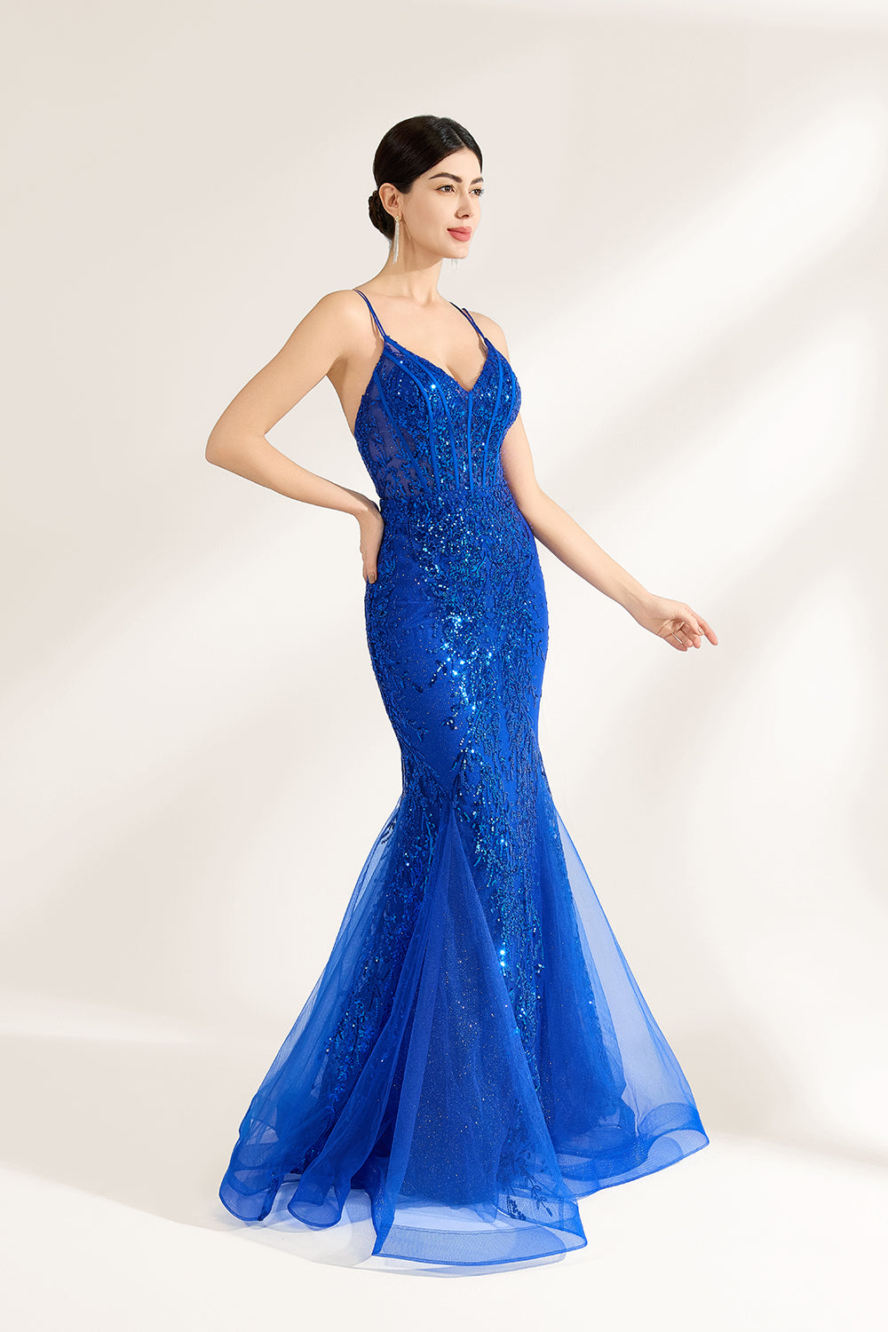 A woman stands against a light background, wearing a royal - blue, sequin - adorned mermaid gown. It features thin straps, a deep V - neckline, and a sheer tulle overlay. The sparkling sequins and figure - hugging silhouette create a glamorous look, perfect for formal events like galas or proms, exuding elegance and charm.3