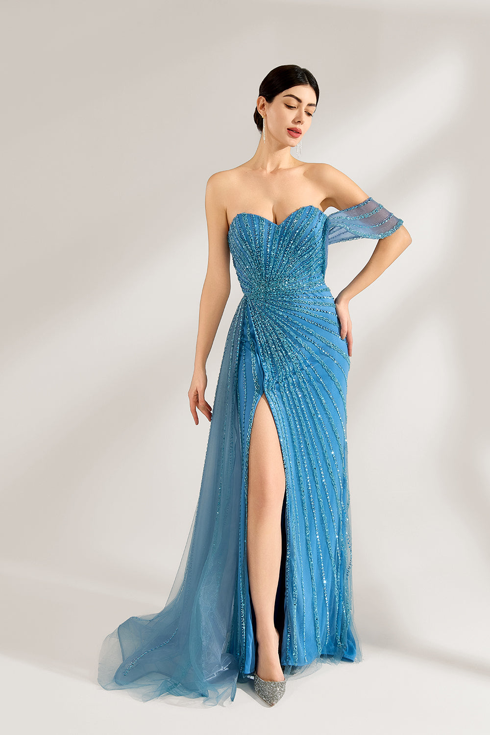 Bathed in soft light, a woman radiates elegance in a blue evening gown. With one - shoulder design, sequin detailing, and a high slit, it crafts a glamorous and sophisticated look for formal events.1