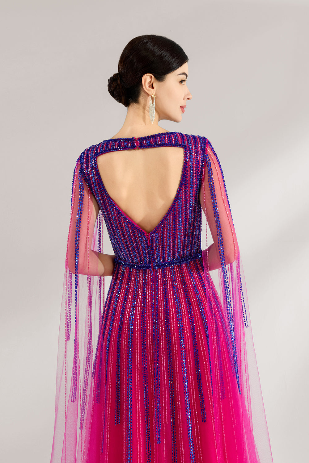 Illuminated softly, a woman enchants in a pink - purple gradient gown. With sequin detailing, a cut - out neckline, and a tulle cape, it creates a magical and elegant look for formal events.7