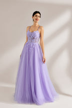 Set against a light backdrop, a woman wears a lavender tulle gown. It has thin straps, a sweetheart neckline with intricate lace embroidery on the bodice, and a flowing tulle skirt. The graceful design gives off a romantic and ethereal vibe, ideal for formal occasions such as proms or weddings.3