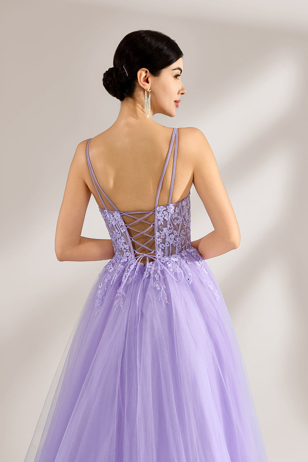 Set against a light backdrop, a woman wears a lavender tulle gown. It has thin straps, a sweetheart neckline with intricate lace embroidery on the bodice, and a flowing tulle skirt. The graceful design gives off a romantic and ethereal vibe, ideal for formal occasions such as proms or weddings.6