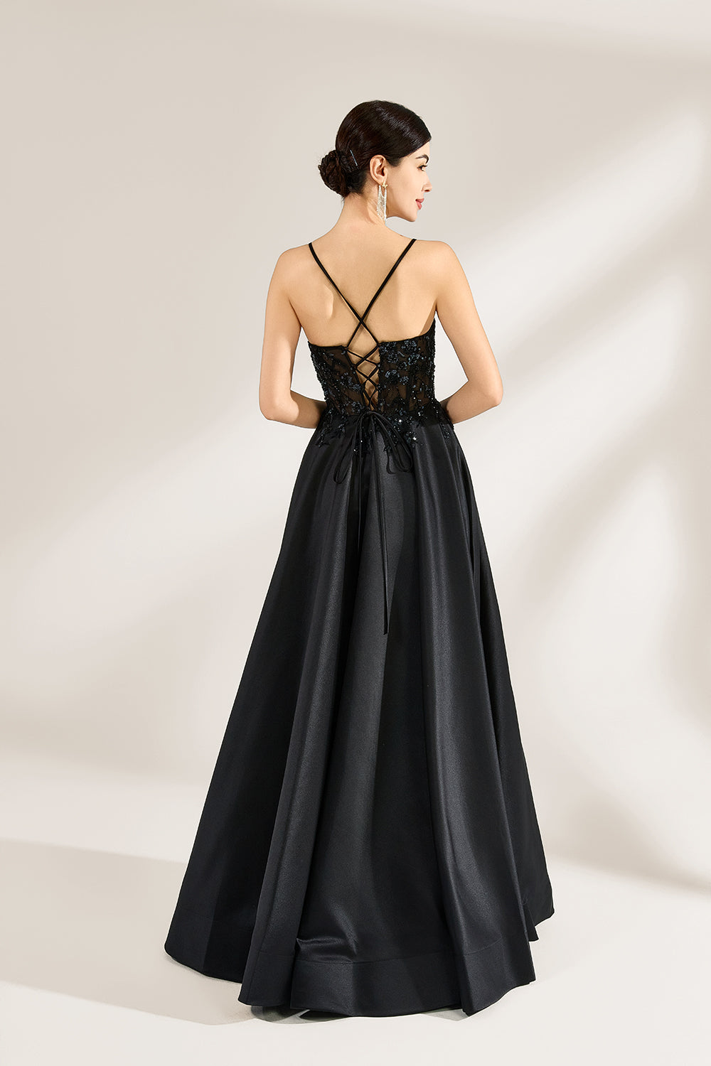 A woman stands against a light background, wearing a black satin gown. The bodice features thin straps, a draped neckline, and beaded embroidery. A high side slit adds allure, combining elegance and sexiness. Perfect for formal events like galas or evening parties, exuding sophistication.2
