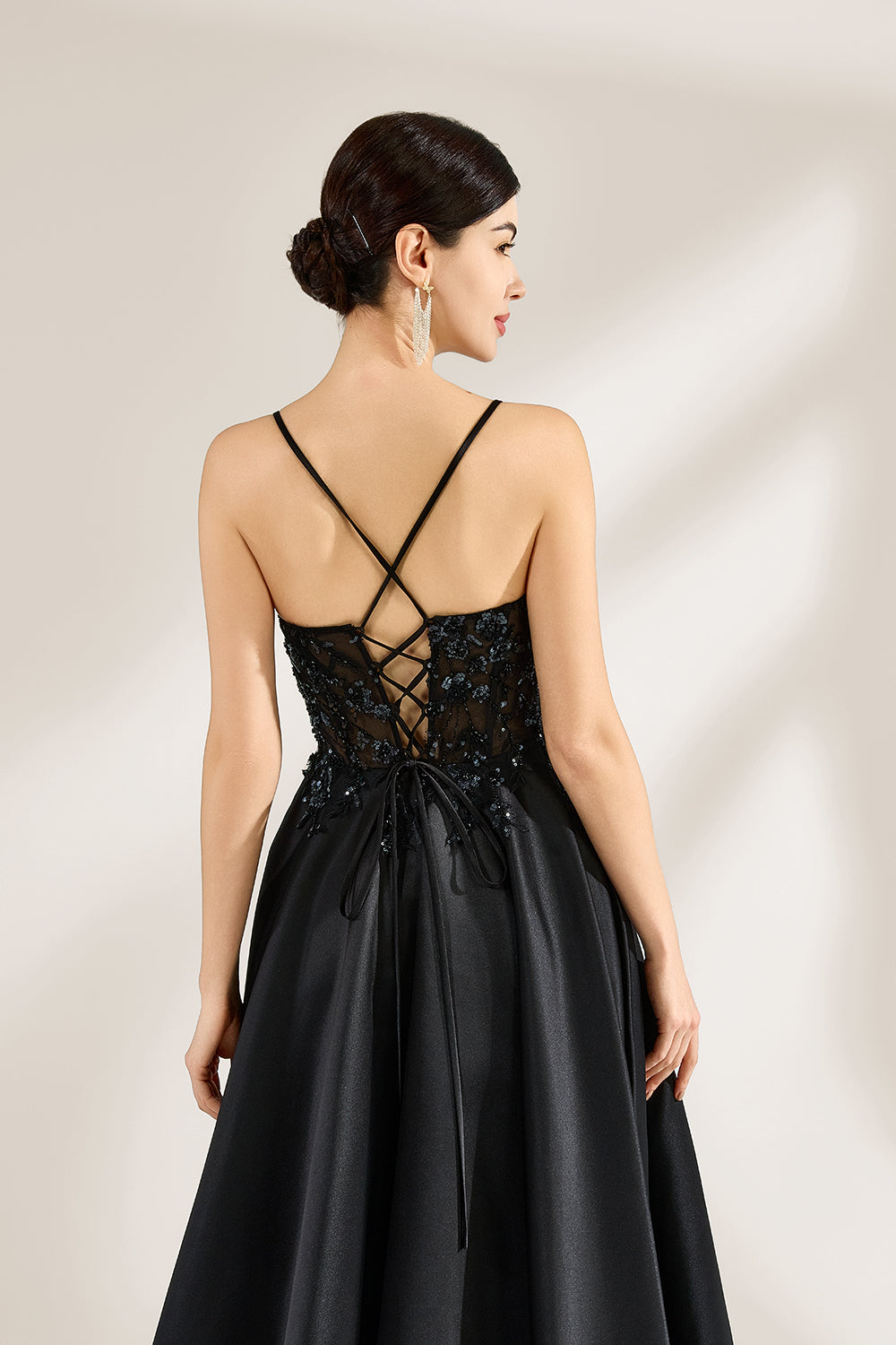 A woman stands against a light background, wearing a black satin gown. The bodice features thin straps, a draped neckline, and beaded embroidery. A high side slit adds allure, combining elegance and sexiness. Perfect for formal events like galas or evening parties, exuding sophistication.7
