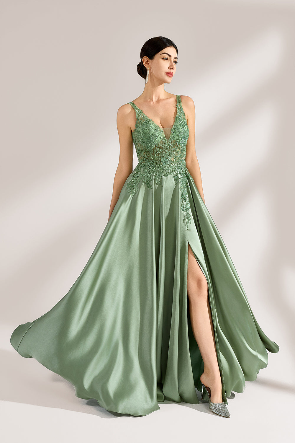 A woman with an elegant updo and a poised stance wears a sage - green satin gown. It has thin straps, a lace - detailed, V - neck bodice, and a high side slit. Paired with silver - tone heels, the outfit radiates grace, perfect for formal events like galas or weddings.3
