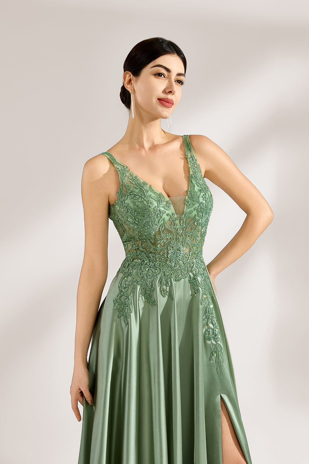 A woman with an elegant updo and a poised stance wears a sage - green satin gown. It has thin straps, a lace - detailed, V - neck bodice, and a high side slit. Paired with silver - tone heels, the outfit radiates grace, perfect for formal events like galas or weddings.4