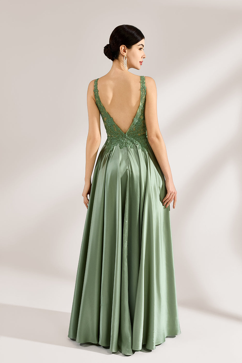 A woman with an elegant updo and a poised stance wears a sage - green satin gown. It has thin straps, a lace - detailed, V - neck bodice, and a high side slit. Paired with silver - tone heels, the outfit radiates grace, perfect for formal events like galas or weddings.5