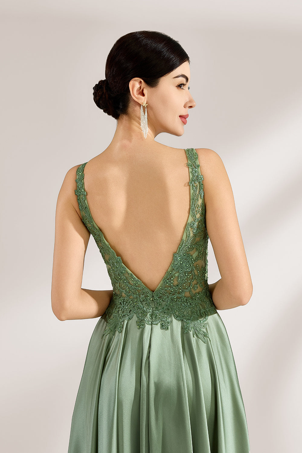 A woman with an elegant updo and a poised stance wears a sage - green satin gown. It has thin straps, a lace - detailed, V - neck bodice, and a high side slit. Paired with silver - tone heels, the outfit radiates grace, perfect for formal events like galas or weddings.6