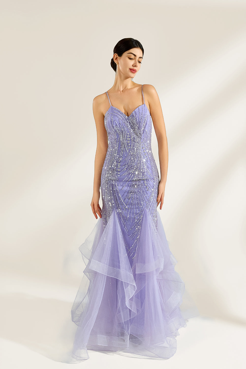 A woman stands against a light background, wearing a lavender mermaid gown. It has thin straps, a deep V - neckline, and is adorned with intricate silver bead patterns. The layered tulle skirt adds a romantic touch, perfect for formal events like galas or weddings, exuding elegance and charm.1